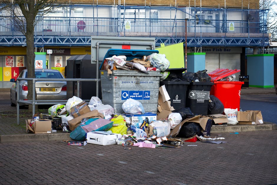 The image shows the rear end of a white commercial van parked on a street, with three large blue rubbish bags positioned on the ground close to the vehicle's tailgate. The bags appear to be filled wit